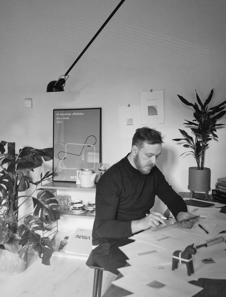 Herman Talvitie working at his design studio desk, surrounded by sketches, design books, and plants